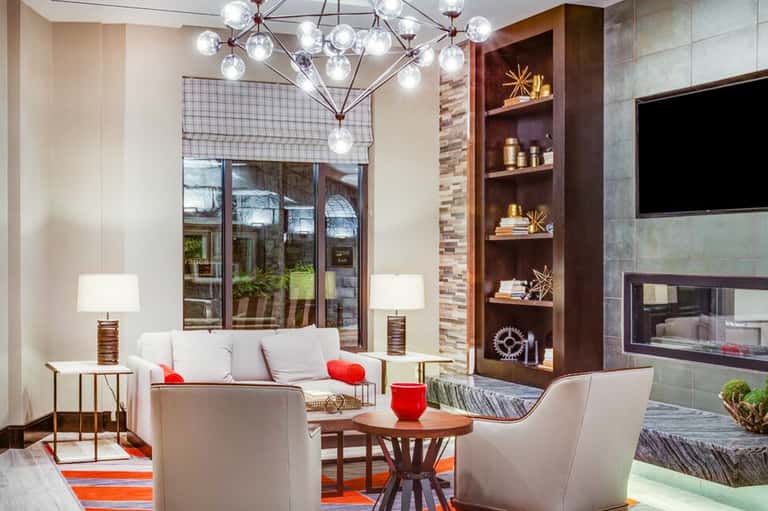 Contemporary hotel lounge with fireplace, artwork displays, pendant chandelier, and window views