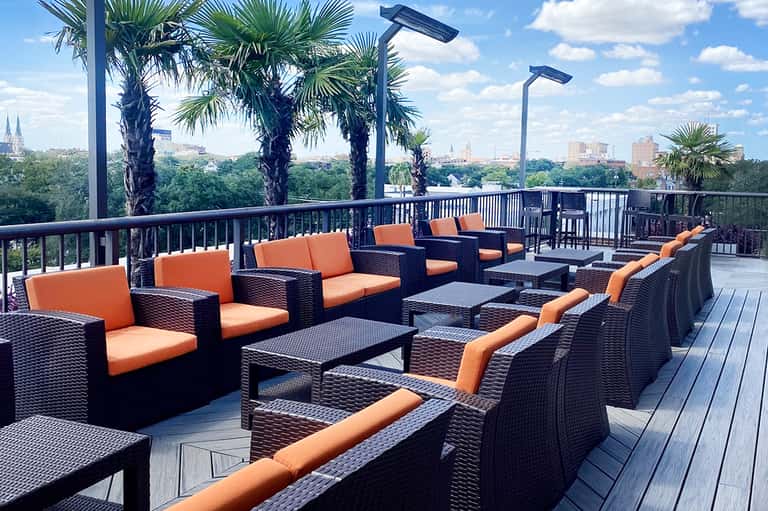 Rooftop lounge with orange cushioned seating, black wicker furniture, and city skyline view