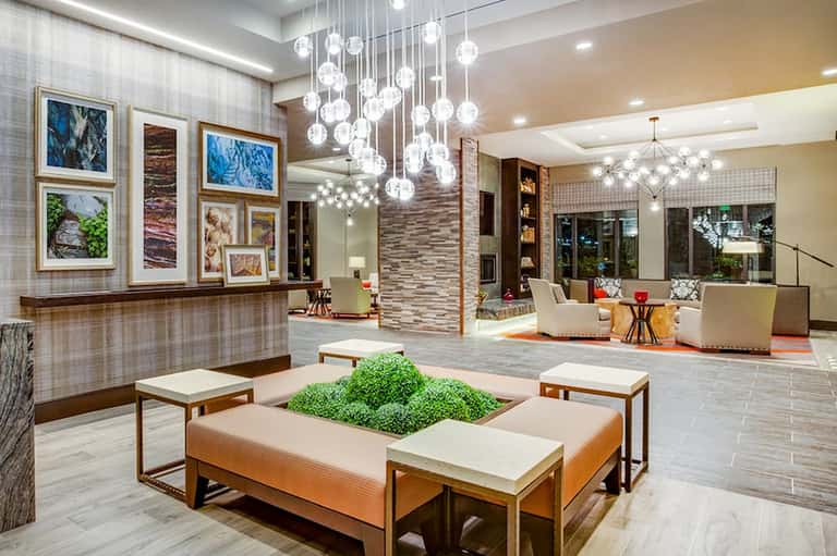 Contemporary hotel lobby with modern chandelier, artwork, and seating area with central green plant feature