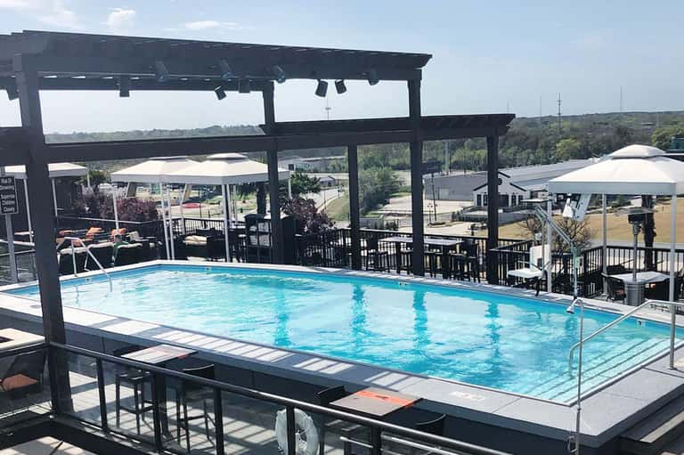 Resort pool with black pergola, white umbrellas, lounge chairs, and scenic overlook of trees and fields