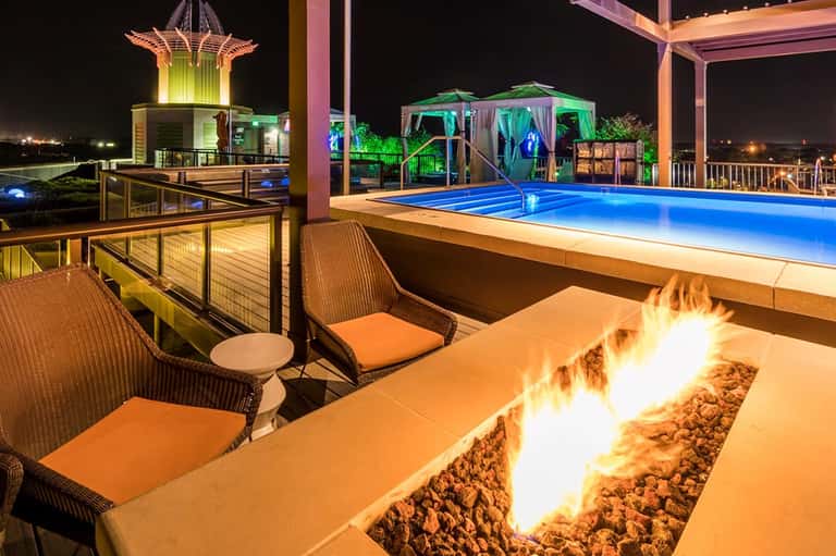 Illuminated pool deck at night with fire pit, lounge chairs, and decorative lighting