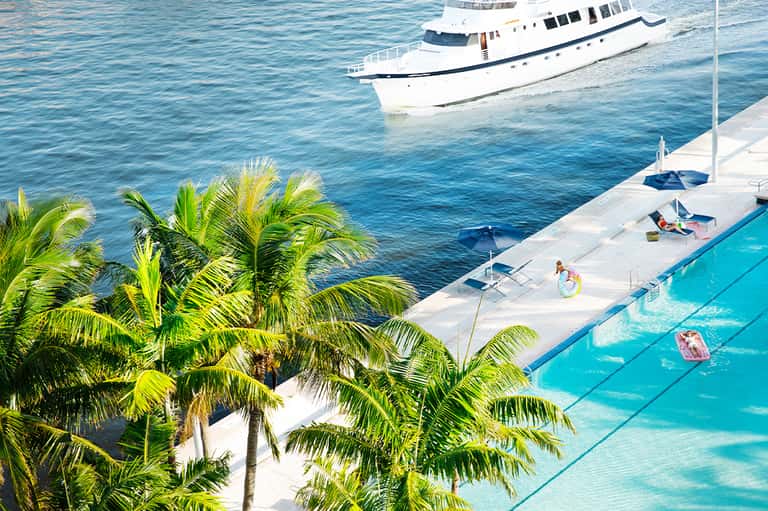 Luxury oceanfront pool deck with yacht moored in turquoise waters and palm trees