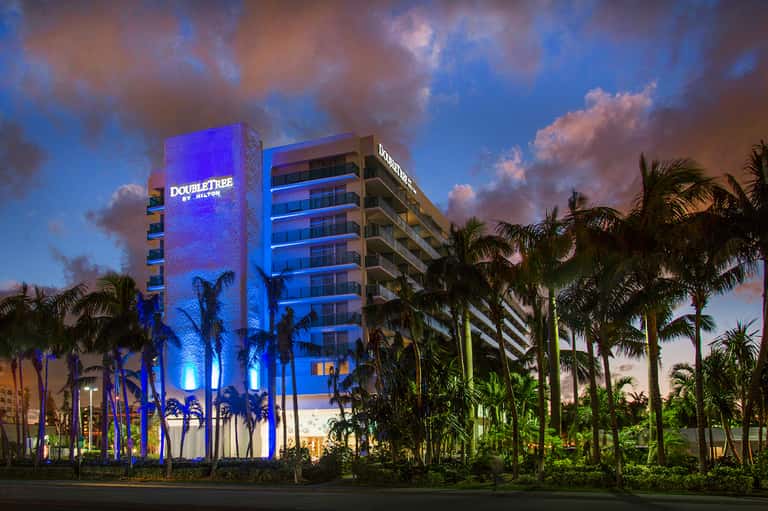 DoubleTree hotel illuminated at dusk with blue lighting, palm trees, and tropical landscaping