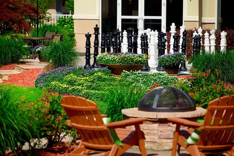 Garden courtyard with fire pit, colorful flowers, and large chess pieces
