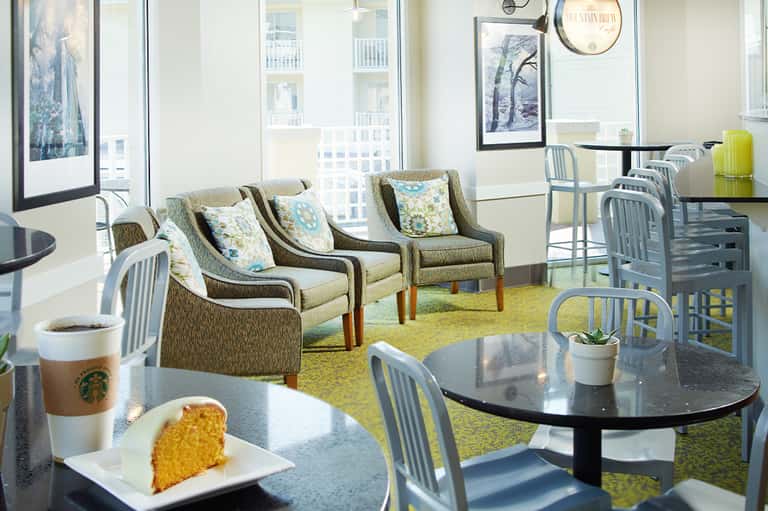 Bright café lounge with upholstered seating, large windows, and high-rise city views