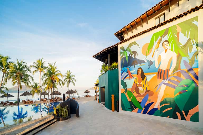 Colorful resort mural overlooking beachfront pool, palm trees, lounge chairs, and ocean