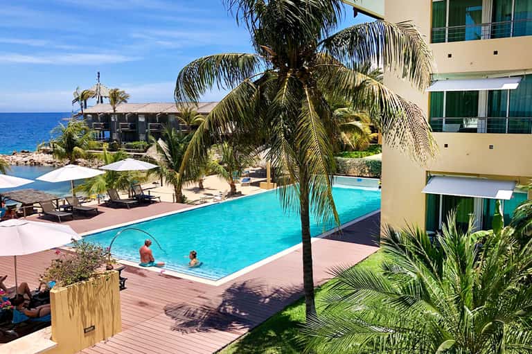 Resort pool with turquoise water, palm trees, and coastal ocean view