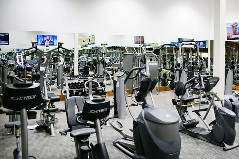 Modern fitness center with rows of Cybex exercise equipment and TV monitors on white walls