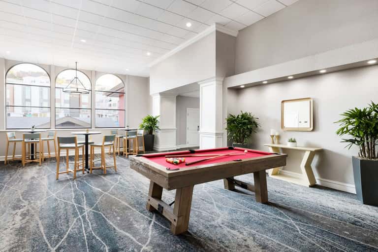 Modern lounge with billiards table, seating areas, arched windows, and contemporary décor