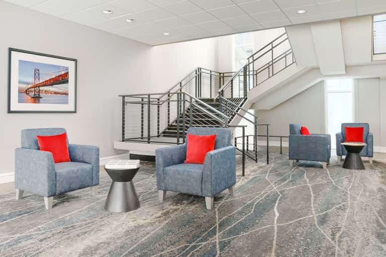 Contemporary lobby lounge with blue armchairs, red pillows, modern staircase, and clean design