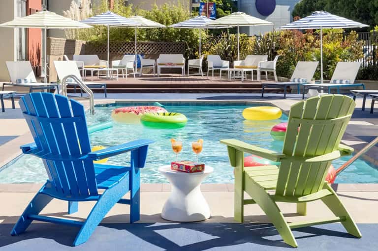 Luxury resort pool with colorful floats, blue and green Adirondack chairs, and shaded lounge areas