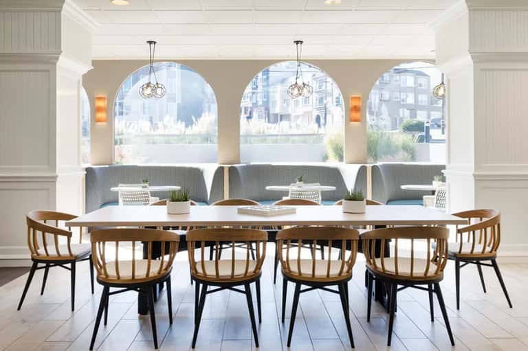 Bright dining room with wooden chairs, long white table, arched windows, and waterfront views