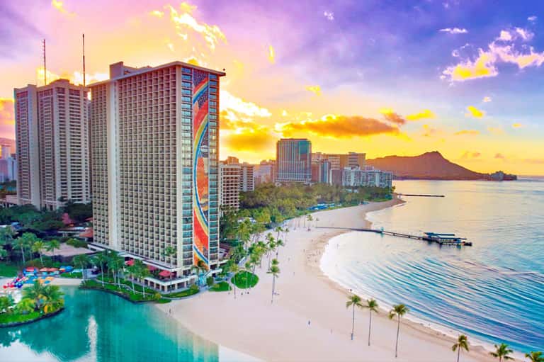 High-rise resort hotel at sunset overlooking sandy beach with Diamond Head mountain