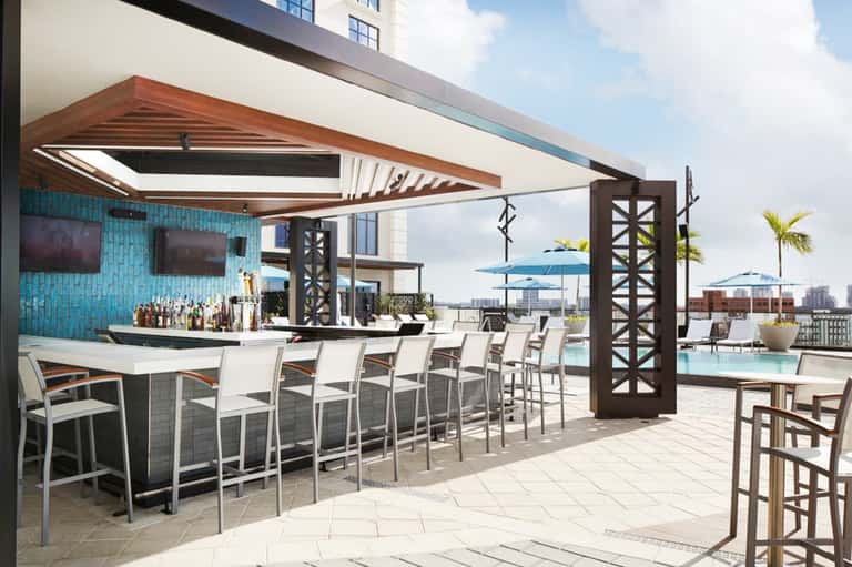 Upscale rooftop bar with turquoise tile, wooden shade structure, and city skyline