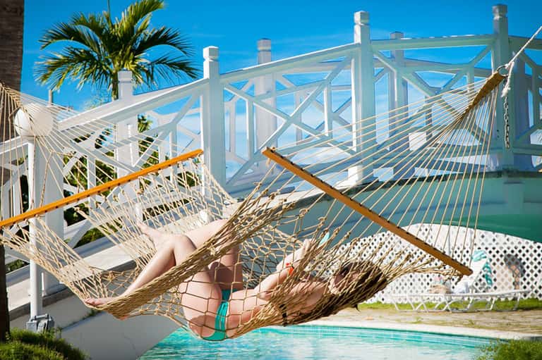 Woman relaxing in woven hammock overlooking ocean with white railing and palm trees