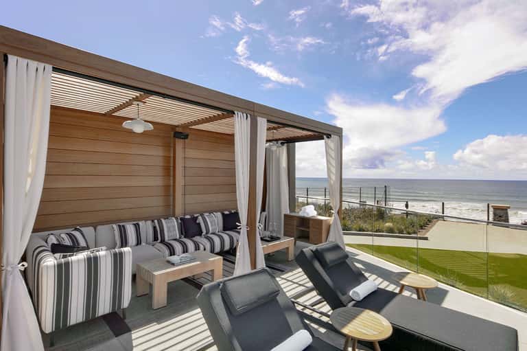 Oceanfront cabana with striped furniture, sheer curtains, lounge chairs, and sea views