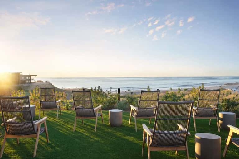 Oceanfront seating area with modern chairs on grass at sunset