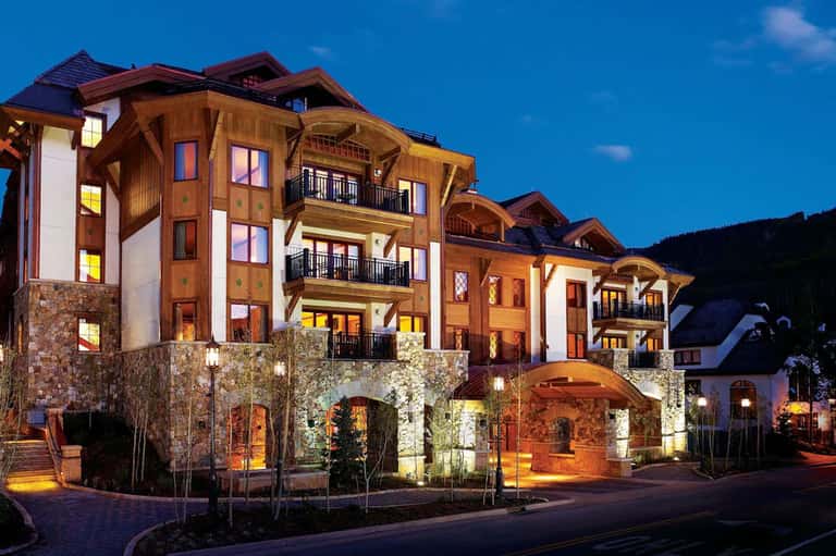 Luxury mountain resort building illuminated at dusk with stone and timber architecture and manicured landscaping