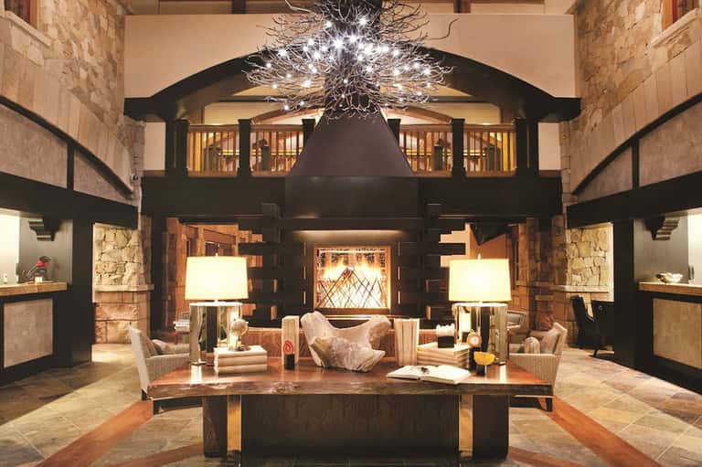 Modern hotel lobby atrium with dramatic branching chandelier, stone walls, and contemporary furnishings