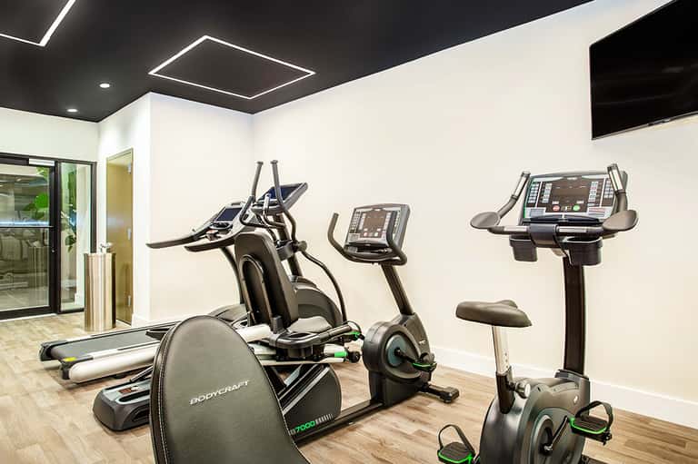 Hotel fitness center with cardio equipment, treadmills, and modern LED ceiling lights
