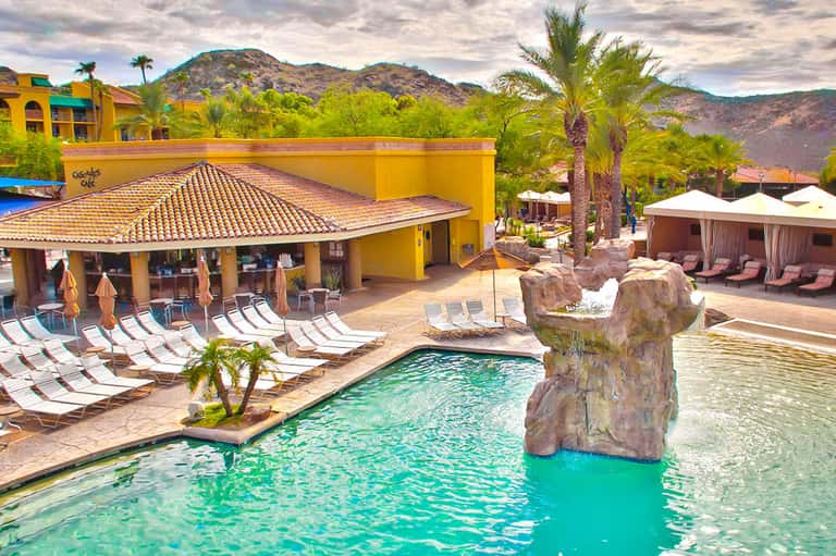 Luxury resort pool area with yellow architecture, lounge chairs, and desert mountains in background