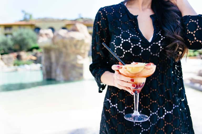Woman in black lace cover-up holding tropical cocktail with grapefruit garnish at resort