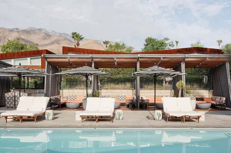 Desert resort pool area with white loungers, striped umbrellas, and mountain backdrop