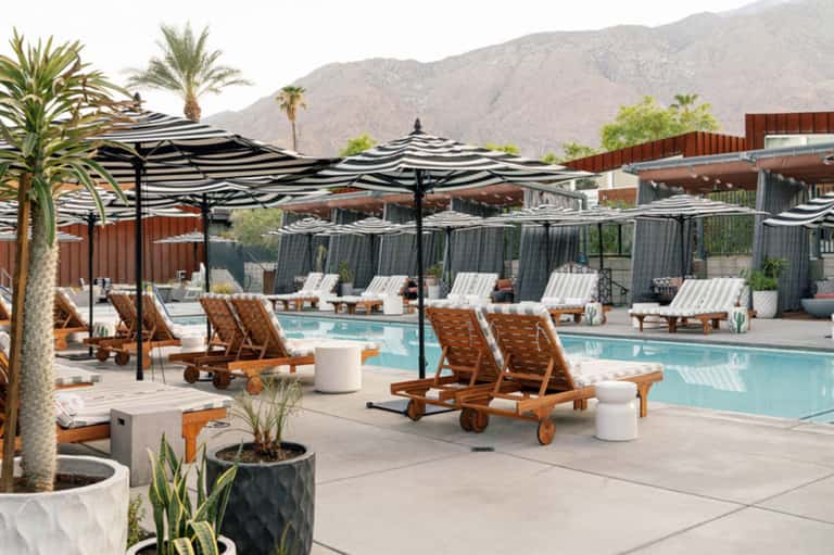 Luxury resort pool with striped umbrellas, loungers, and desert mountain backdrop