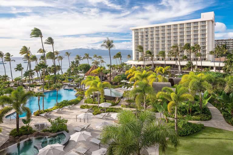 Oceanfront resort with multiple pools, palm trees, and mountains in background