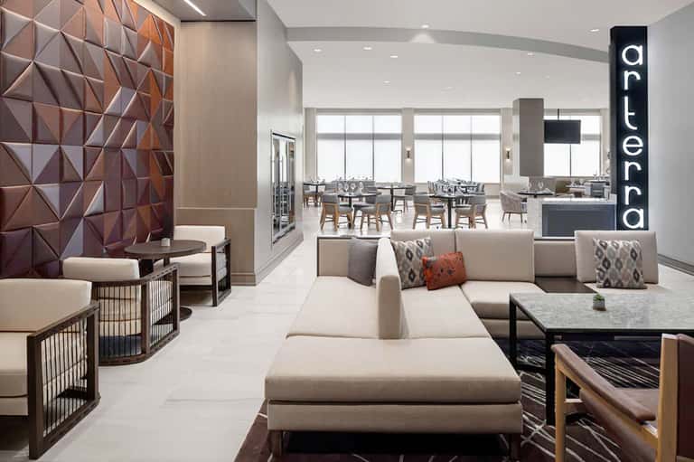 Contemporary hotel lounge with beige seating, textured wall art, and dining