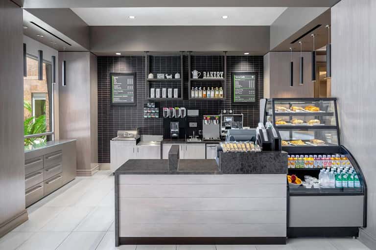 Modern bakery café interior with black tiled walls, espresso machine, pastry display cases, and minimalist contemporary design