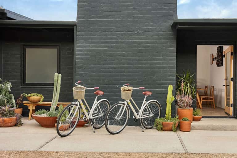 Modern black home exterior with bicycles parked outside and potted cacti decoration