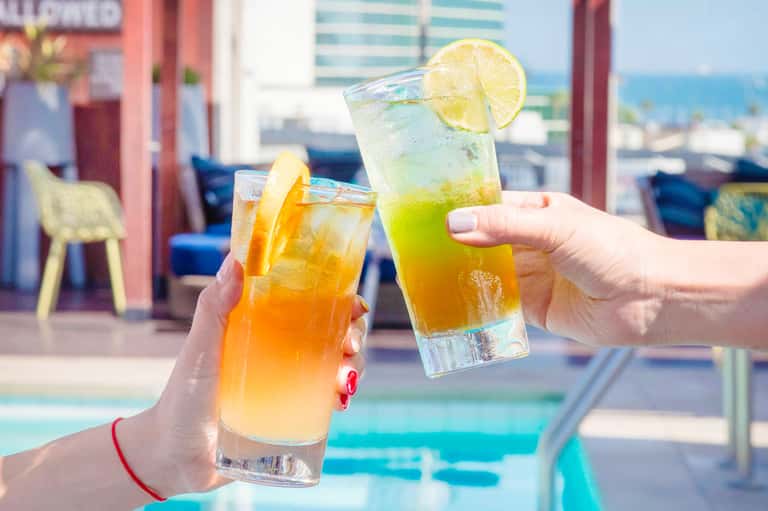 Two colorful cocktails with citrus garnishes by a poolside overlooking the ocean