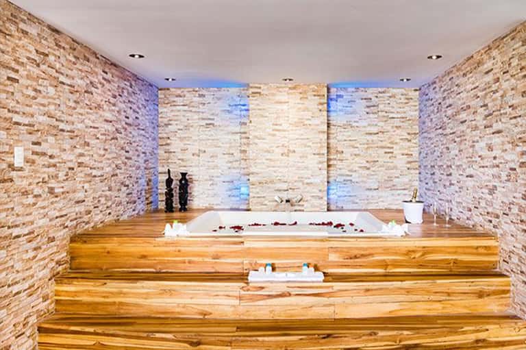 Spa bathtub with rose petals, candles, and brick accent walls with blue lighting