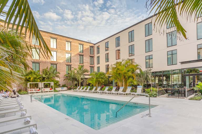 Courtyard pool surrounded by palm trees, white loungers, and brick hotel building