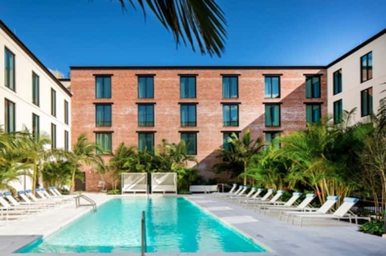 Outdoor courtyard pool surrounded by brick building with palm trees and loungers