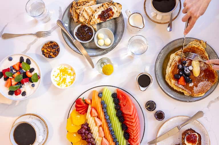 Overhead view of brunch spread with pancakes, fresh fruit platter, coffee, and morning drinks