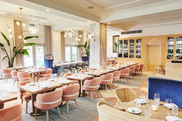 Modern fine dining restaurant with coral chairs, wooden tables, and contemporary chandeliers