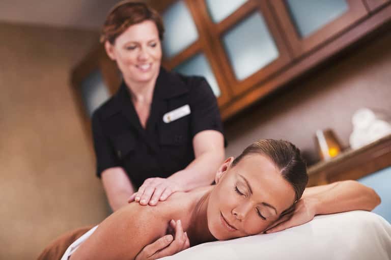 Spa therapist performing shoulder massage on relaxed guest in treatment room