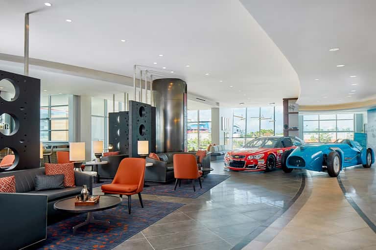 Luxury hotel lobby with modern furniture, sports car displays, and expansive glass windows