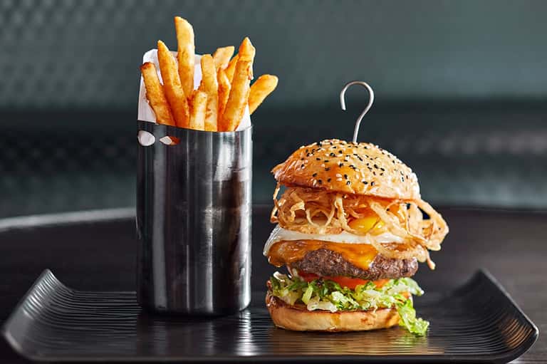 Gourmet burger with crispy fries in a metal cup on a black plate