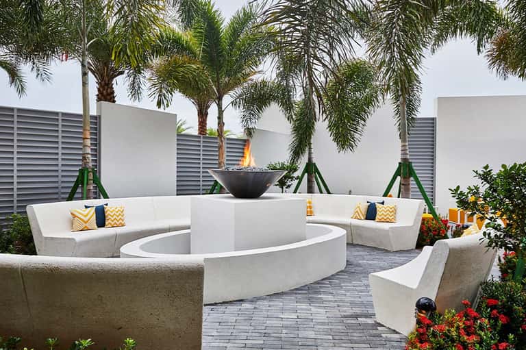 Resort fire pit lounge area with curved white seating, palm trees, and decorative pillows