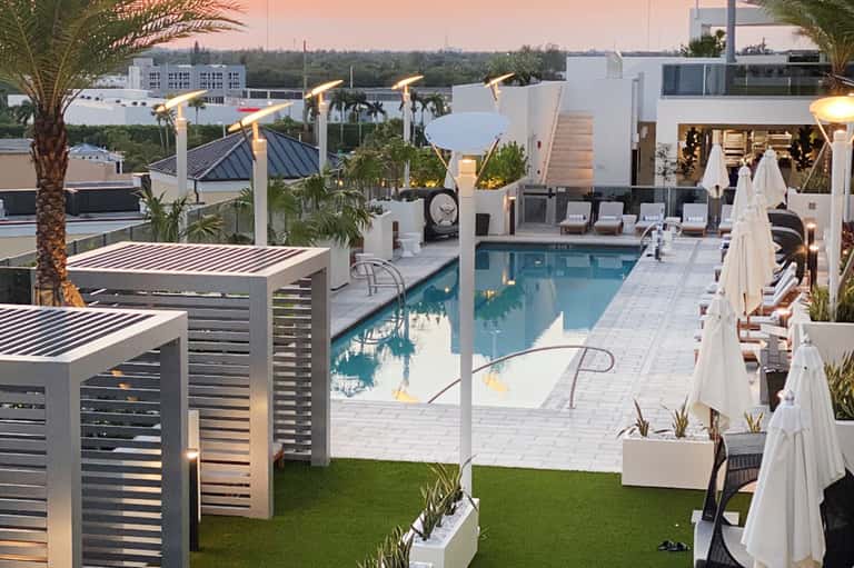 Elevated view of luxury rooftop pool at dusk with modern white loungers, heaters, and city skyline