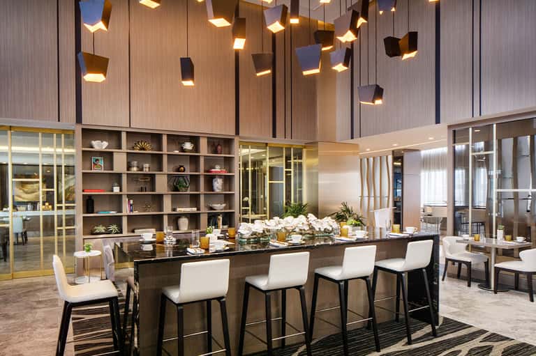 Contemporary dining space with long black table, white chairs, pendant lighting, and floor-to-ceiling windows
