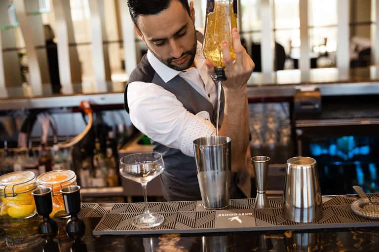 Bartender in vest and white shirt pouring cocktail at upscale bar counter