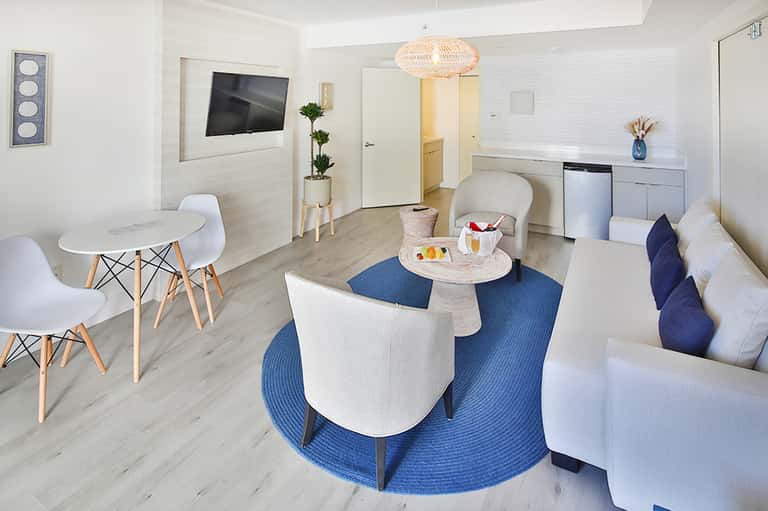 Modern hotel suite with white furniture, kitchenette, and contemporary decor