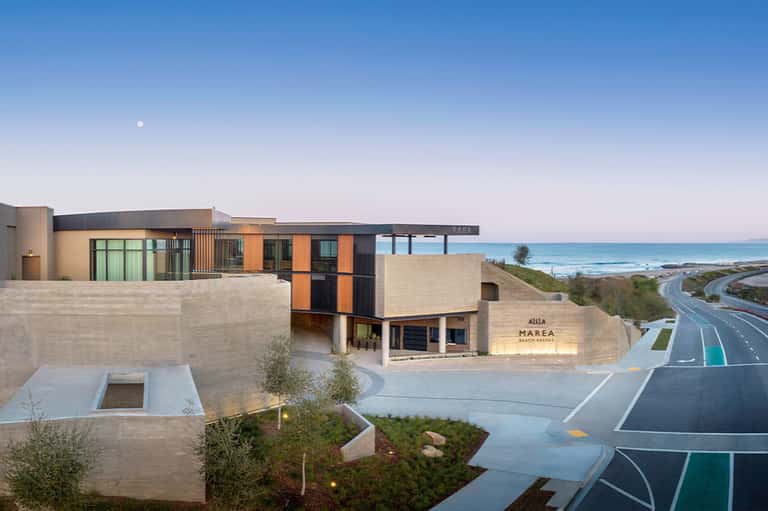 Modern beach resort building with beige stone, orange and black metal panels overlooking ocean and coastline