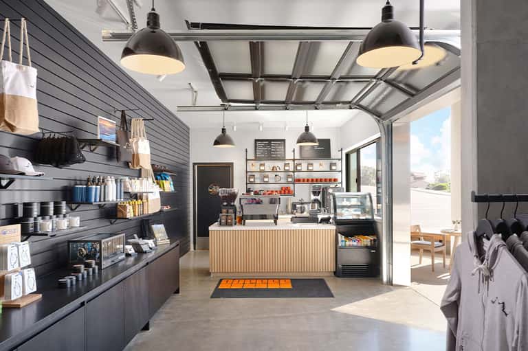 Modern coffee shop interior with black pendant lights, black shiplap walls, shelving displays, and glass garage doors