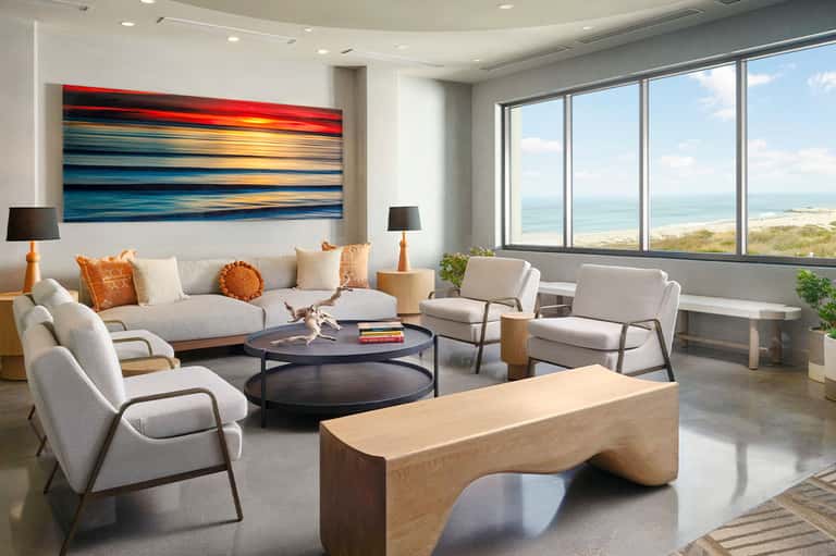 Modern living room with ocean view windows, neutral furniture, abstract artwork and contemporary design