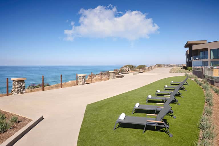 Oceanfront property with lounge chairs on lawn, beach access, and modern building architecture